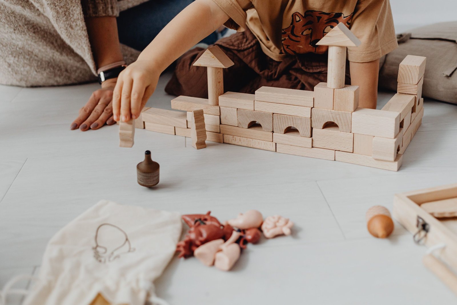 A child playing with wooden blocks and toys on a light-colored floor indoors.